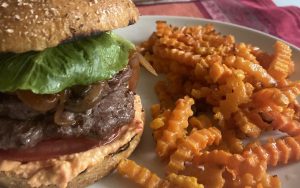 These venison burgers on the grill – with a spicy cheese sauce and browned onions and mushrooms – help spice up the summer.  Image