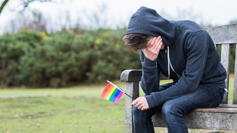sad teenage boy holding pride flag photo by Ben Gingell Dreamstime. After he wears a gown to his prom, Grandma worries about the safety of her gay grandson. Is he going through a phase? See “Ask Amy” says. Image
