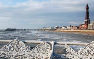 Blackpool is a carnival-esque tipsy-toupee, ears-pierced-while-you-wait place, where I can experience working-class England at play. Showing its beach and tower. Image