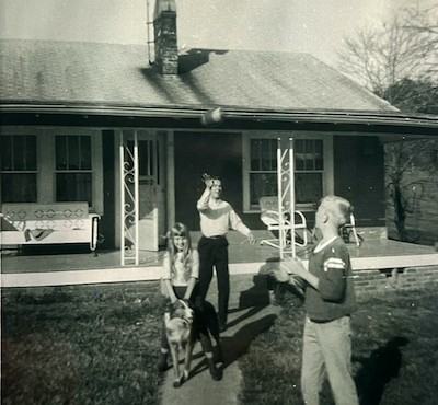 Julia and Laddie c. 1964, for Julia Nunnally Duncan's poem, "True Friend." Duncan says, "The photo is of me with my collie Laddie, taken around 1964, at our neighbors’ house. My older brother Steve is the blond boy wearing the ball jersey and our neighbor Ray is throwing the ball to Steve."