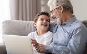 granddad and grandson on a laptop, laughing, possibly playing puzzles like Boggle and Jumble. Image by Fiszkes, Dreamstime. Image