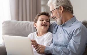 granddad and grandson on a laptop, laughing, possibly playing puzzles like Boggle and Jumble. Image by Fiszkes, Dreamstime. Image