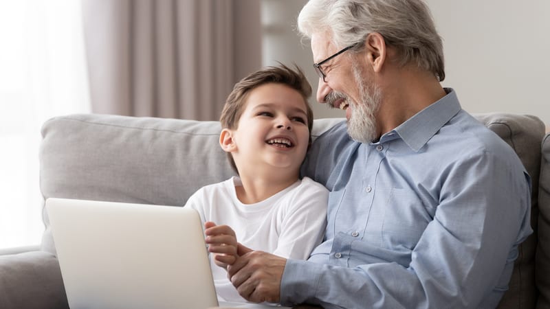 granddad and grandson on a laptop, laughing, possibly playing puzzles like Boggle and Jumble. Image by Fiszkes, Dreamstime. Image