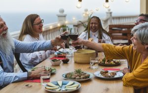multiracial senior friends at a table outside, with food and wine, laughing. Alessandro Biascioli Dreamstime. Boomer reader Kate M. Carey bemoans little aches and pains, remedies, and early evenings that infiltrate life with her husband and friends. Image