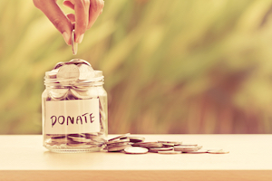 Hand putting Coins in glass jar with DONATE word written text label for giving and donation concept