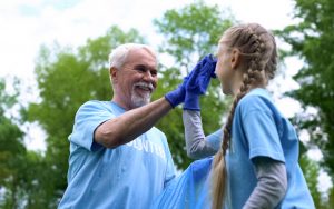 Senior man volunteering at a park clean-up event, high-fiving a young girl who is also volunteering. Looking for wise ways to use your retirement? Consider these 5 ways to give back and make your community and the world a better place. Image