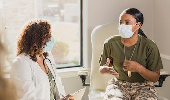 female soldier at a doctor's visit. For article on Resources are available to help veterans managing IBD (inflammatory bowel disease), such as Crohn’s disease and ulcerative colitis. Image by Getty Images, via Family Features.