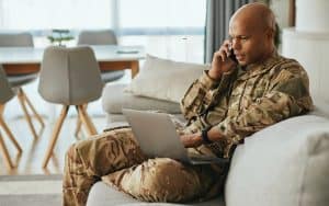 Soldier sitting and talking on a phone while also looking at a laptop for resources, such as resources are available to help veterans managing IBD (inflammatory bowel disease), such as Crohn’s disease and ulcerative colitis. Image courtesy of Getty Images via Family Features. Image