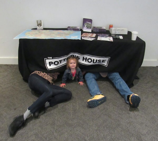 Two pair of adult legs and a child's head peeking out from under a table at The Potter's House (where Bela and Stephen had their final book signing for 'Pilgrim Maya' on their book tour.)
