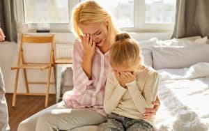 crying mother and daughter sitting on a bed. Photo by Albertshakirov. A concerned grandma wants her daughter, two grandkids, and verbally abusive son-in-law to move in with her. See what “Ask Amy” advises.  Image