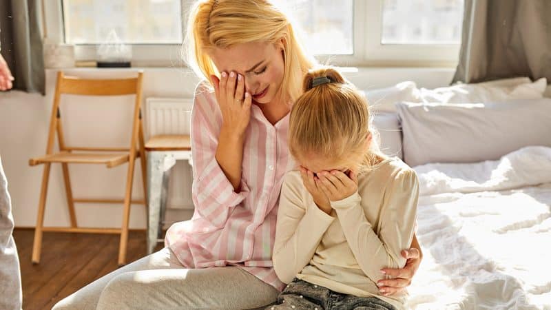 crying mother and daughter sitting on a bed. Photo by Albertshakirov. A concerned grandma wants her daughter, two grandkids, and verbally abusive son-in-law to move in with her. See what “Ask Amy” advises.  Image