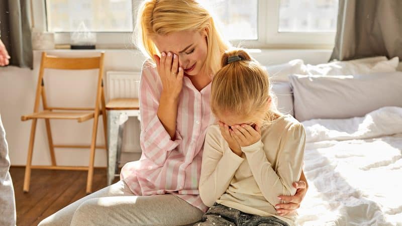 crying mother and daughter sitting on a bed. Photo by Albertshakirov. A concerned grandma wants her daughter, two grandkids, and verbally abusive son-in-law to move in with her. See what “Ask Amy” advises. Image