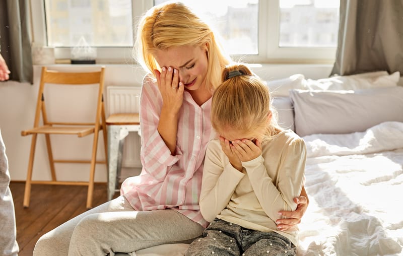 crying mother and daughter sitting on a bed. Photo by Albertshakirov. A concerned grandma wants her daughter, two grandkids, and verbally abusive son-in-law to move in with her. See what “Ask Amy” advises. 