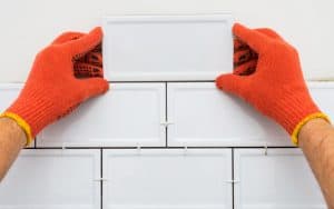 A worker's hands laying new tile. The pandemic seemed the perfect time to tackle a kitchen renovation, but Covid disagreed! Allan Ripp shares the tale from his NYC apartment. Image