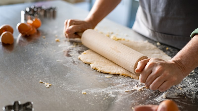 woman using a rolling pin to roll out dough. Image by Lido. Her husband asked her to prepare additional baked goods for a gluten-free guest, but she’s feeling a bit overwhelmed. See what “Ask Amy” says.