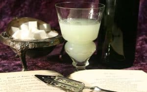 Absinthe and sugar cubes beside an open book of Edgar Allan Poe poems. For article on Edgar Allan Poe-inspired tipples. Image