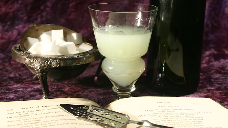 Absinthe and sugar cubes beside an open book of Edgar Allan Poe poems. For article on Edgar Allan Poe-inspired tipples. Image