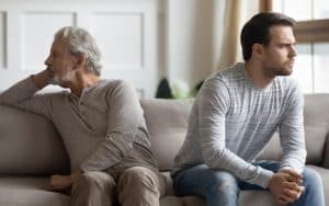 troubled father and his adult son on a couch. By Fizkes. A father suspects that one of his sons was the result of his ex-wife’s affair. Now, this dad desires DNA disclosure. See what “Ask Amy” says. Image