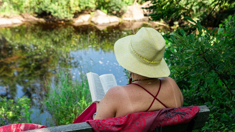 Woman reading a book outside by a pond. By Valmedia Creatives. Becoming healthier can seem intimidating, but these 10 easy, healthy actions to do regularly can make a world of difference.