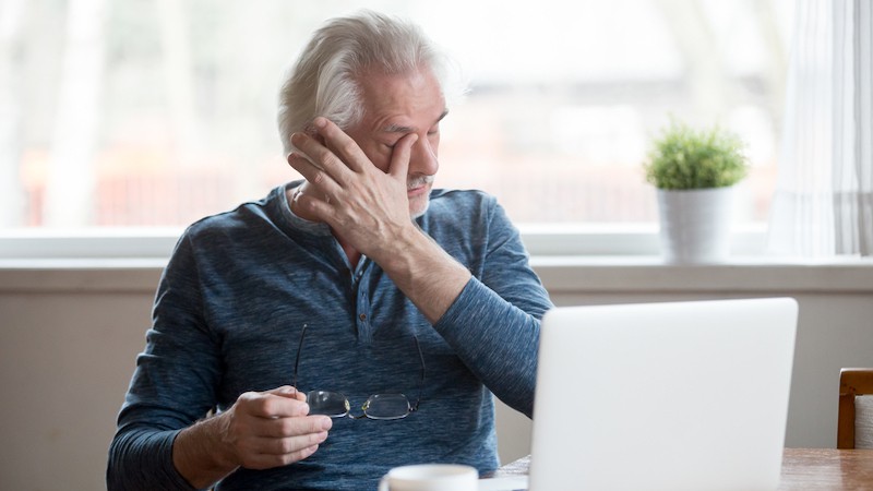 man with tired eyes, rubbing his eyes, from eyestrain from computer. By Fizkes. Blue light-blocking glasses are said to benefit the eyes by blocking blue light from electronics. Are they really useful or simply hype?