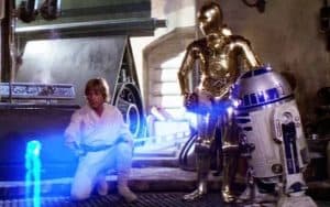 Luke Skywalker, C-3PO, and R2-D2, looking at a hologram in the movie 