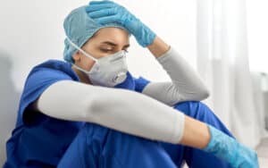 a sad nurse or doctor wearing PPE and sitting on the floor of a hospital. Image by Syda Productions. A nurse is tired of hearing people complain about working from home. See what “Ask Amy” says about post-pandemic problems and perspectives. Image