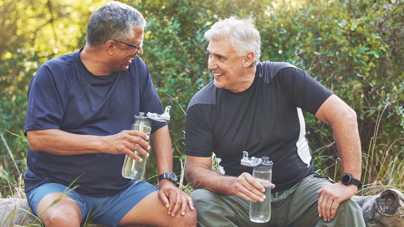 two men drinking water after outdoor fitness. Image by Yuri Arcurs. Article on 10 pampering fitness tips.