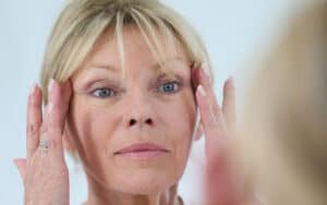 a woman looking at her wrinkles in the mirror. By Goodluz. A Boomer reader reflects on the images of her life, especially the image of her face in a make-up mirror, which has stayed with her since her teen years. Image