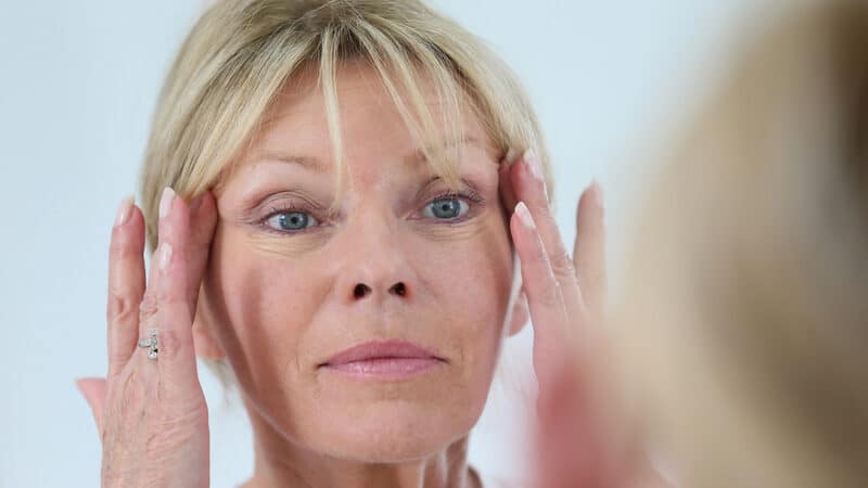 a woman looking at her wrinkles in the mirror. By Goodluz. A Boomer reader reflects on the images of her life, especially the image of her face in a make-up mirror, which has stayed with her since her teen years. Image