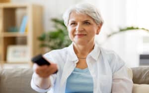 older woman watching TV and smiling, by Syda Productions. A retired woman is rethinking a self-imposed rule about when to read books and when to watch TV. See what “Ask Amy” says about books vs. TV. Image