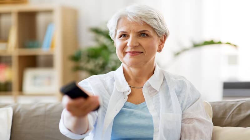 older woman watching TV and smiling, by Syda Productions. A retired woman is rethinking a self-imposed rule about when to read books and when to watch TV. See what “Ask Amy” says about books vs. TV. Image