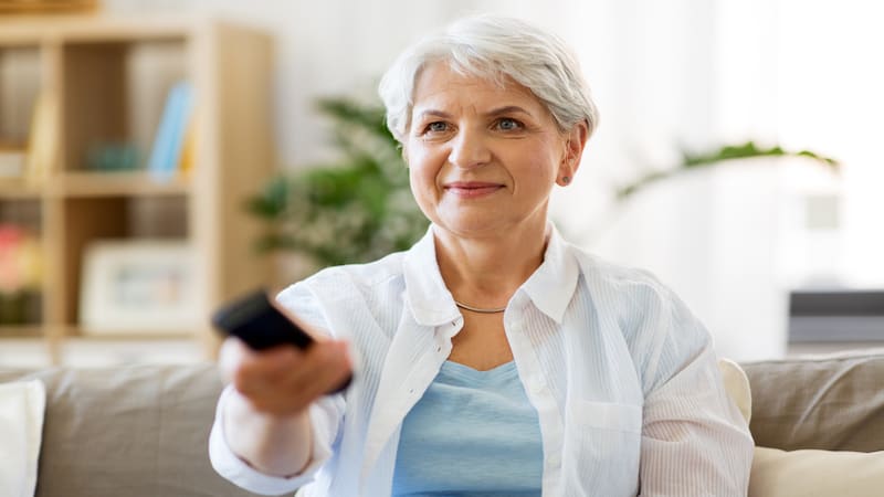 older woman watching TV and smiling, by Syda Productions. A retired woman is rethinking a self-imposed rule about when to read books and when to watch TV. See what “Ask Amy” says about books vs. TV.