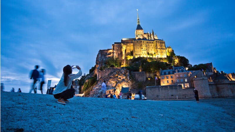Christian pilgrims and tourists are drawn to the dramatically situated Mont St-Michel, a soaring island abbey in Normandy that is completely surrounded by the sea at high tide. The towering abbey of Mont St-Michel rises above the surrounding landscape – which becomes a waterscape at high tide. Traveler Rick Steves takes us to the historic island abbey with its rich history, traditional omelets, and a man-powered treadwheel. Image