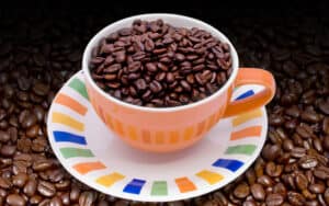 Colombian coffee beans in a colorful cup and saucer, surrounded by more beans; from Victor Habbick. for article on Colombian coffee shop culture Image