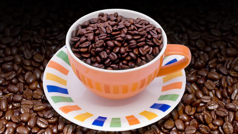 Colombian coffee beans in a colorful cup and saucer, surrounded by more beans; from Victor Habbick. for article on Colombian coffee shop culture