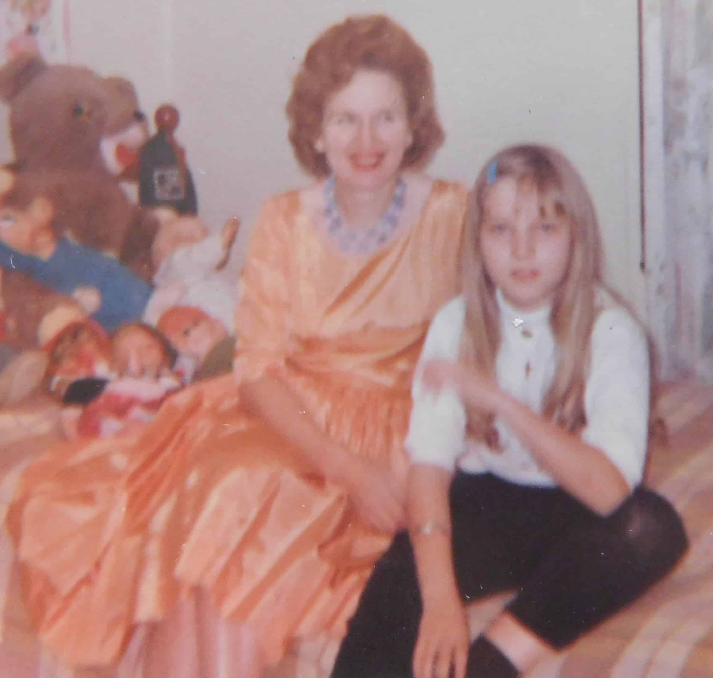 1950s picture of fashionable mother sitting on her daughter's bed, with daughter and stuffed animals.