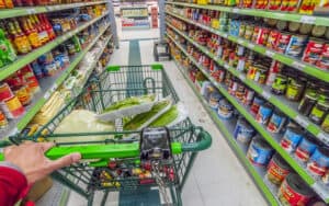 grocery store aisle with a hand pushing a cart, from Helgidinson. Perhaps you’ve done this yourself, imagining the life stories of strangers. Humorist Greg Schwem shares his version of the game. Image