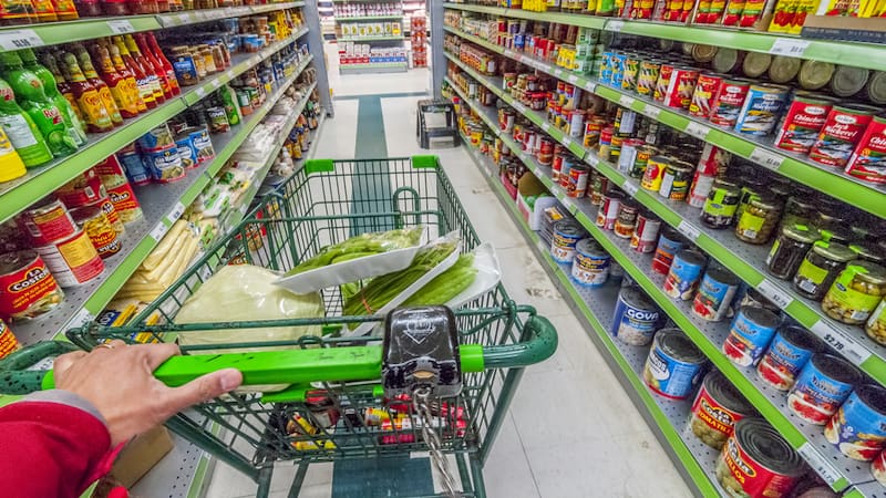 grocery store aisle with a hand pushing a cart, from Helgidinson. Perhaps you’ve done this yourself, imagining the life stories of strangers. Humorist Greg Schwem shares his version of the game.