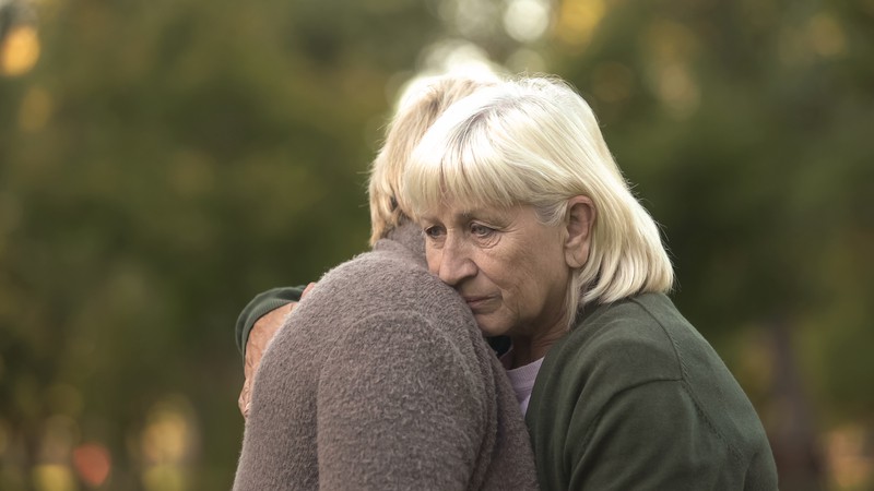 Sad middle-aged women hugging, by motortion. For article on considering a DNA disclosure and family secrets.