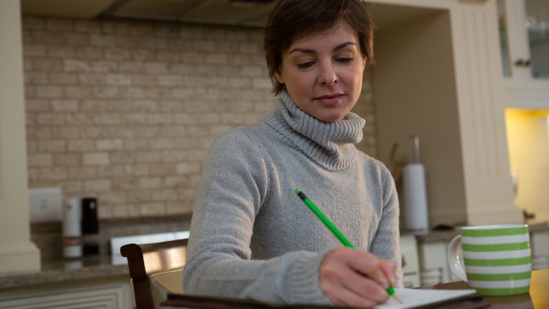 woman writing on a pad at her kitchen table, from Wavebreakmedia Ltd. For article on writing, three-by-five cards and more