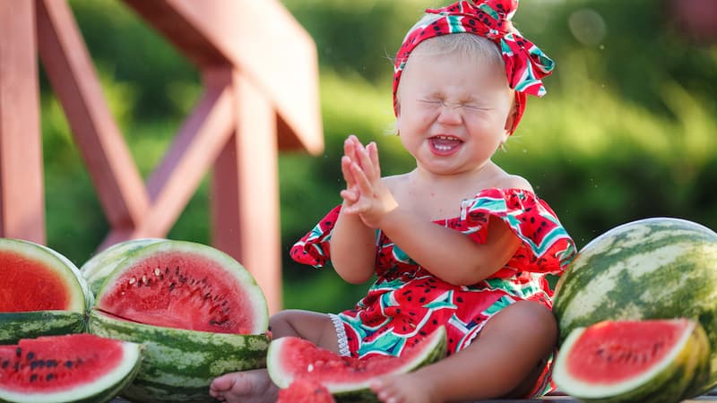 baby girl in watermelon decorated clothing, surrounded by watermelons. By Golyak.