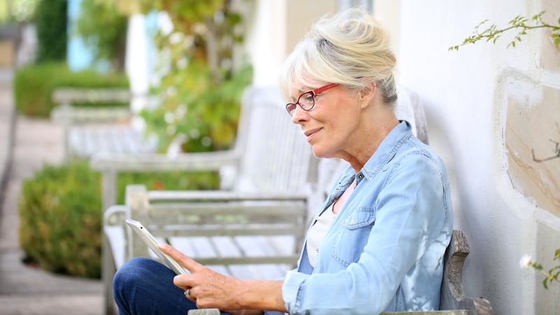 woman sitting outside looking at a tablet, perhaps doing a puzzle like Boggle's Find 7 States