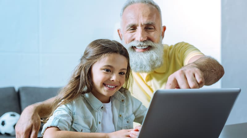 A granddad and granddaughter on a laptop, possibly doing a puzzle like the Boomer Jumble puzzles for kids and adults. Image from Dmytro Zinkevych