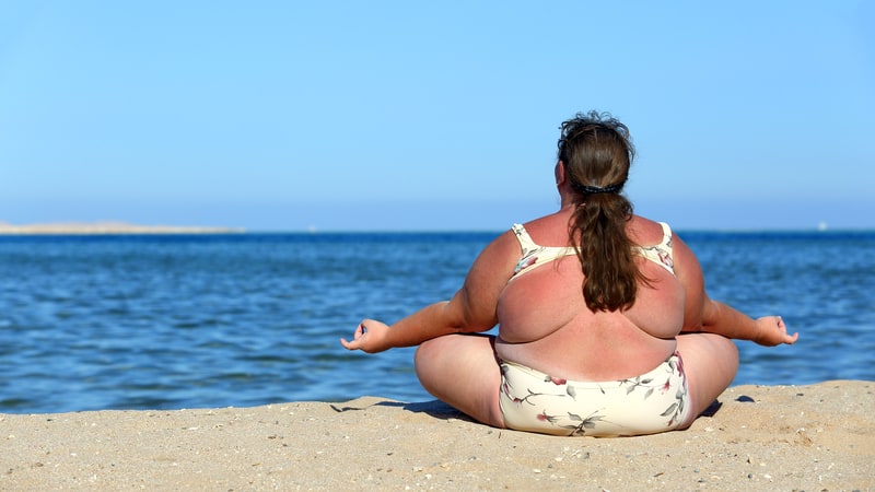 overweight woman meditating at the beach by the water. By Mikhail Kokhanchikov. For article on a mother bothered by her grown daughter's weight