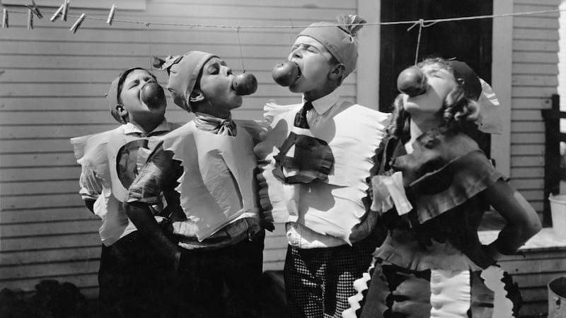 Old picture of children dressed up in costumes and playing an apple-eating contest, by Everett Collection Inc. Article on Halloween memories