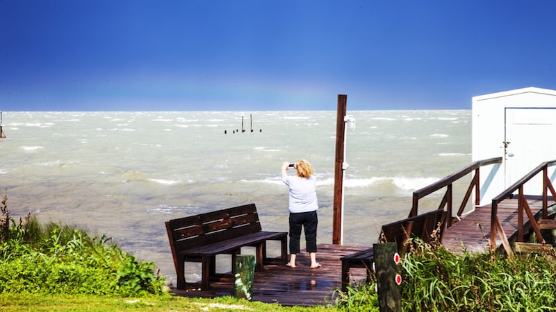 A woman taking a picture of a rainbow in the distance over the Gulf of Mexico, contributed for her article on swan songs