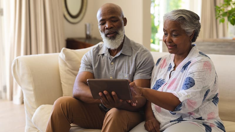 A couple looking at a tablet, at home on their sofa. For use with Boggle find the mammals puzzle