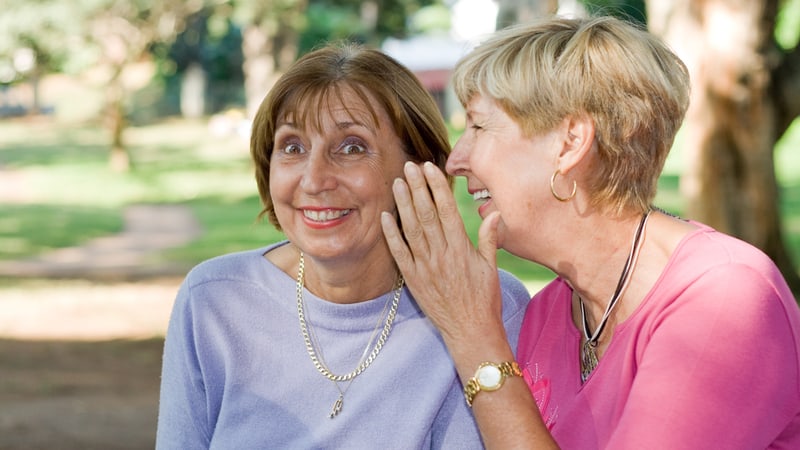 two women outside, engaged in conversation: insensitive friends gossiping to each other.