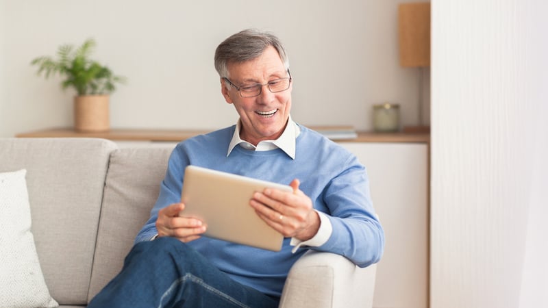 A happy man looking at a computer tablet, maybe even doing some puzzles and games on his device