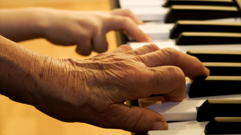 Two hands playing a piano: a young child and an elderly person. For article on Old Things v. Young Ones